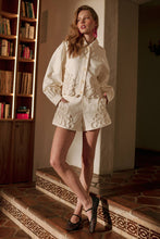 Load image into Gallery viewer, Model wearing écru tailored shorts with oversized floral appliqué embroidery paired with coordinating top in a soft neutral ivory/yellow tone.
