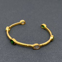 Load image into Gallery viewer, 18K gold-plated open cuff bangle with a hammered textured finish and oval emerald-green and clear zircon stones in gold settings.
