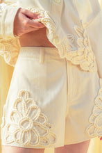Load image into Gallery viewer, Model wearing écru tailored shorts with oversized floral appliqué embroidery paired with coordinating top in a soft neutral ivory/yellow tone.
