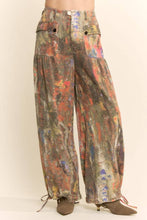 Load image into Gallery viewer, Model wearing abstract print wide leg cargo pants featuring earthy multicolor tones, oversized flap pockets, adjustable tie hems, and a relaxed fit.
