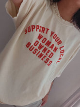 Load image into Gallery viewer, Cream 100% cotton graphic T-shirt with bold red lettering reading "Support Your Local Woman-Owned Business," shown on a model wearing the relaxed-fit tee.
