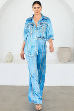 Load image into Gallery viewer, Woman wearing a light blue denim effect blouse and pants set in a minimalistic setting.
