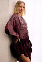 Load image into Gallery viewer, Model wearing burgundy asymmetric ruffle mini skirt with dramatic cascading layers and an elongated side panel, styled with a matching burgundy jacket
