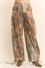 Load image into Gallery viewer, Model wearing abstract print wide leg cargo pants featuring earthy multicolor tones, oversized flap pockets, adjustable tie hems, and a relaxed fit.
