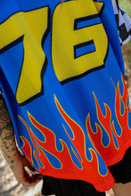 Load image into Gallery viewer, Woman wearing the All American Racing Team oversized mesh jersey featuring blue racing graphics, checkered sleeves, flame details, varsity lettering, and a large number 76 on the back.
