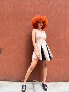 A sleeveless beige mini dress featuring a boat neckline and contrast black accents peeking through the pleats, creating a chic and versatile look suitable for any occasion. 
