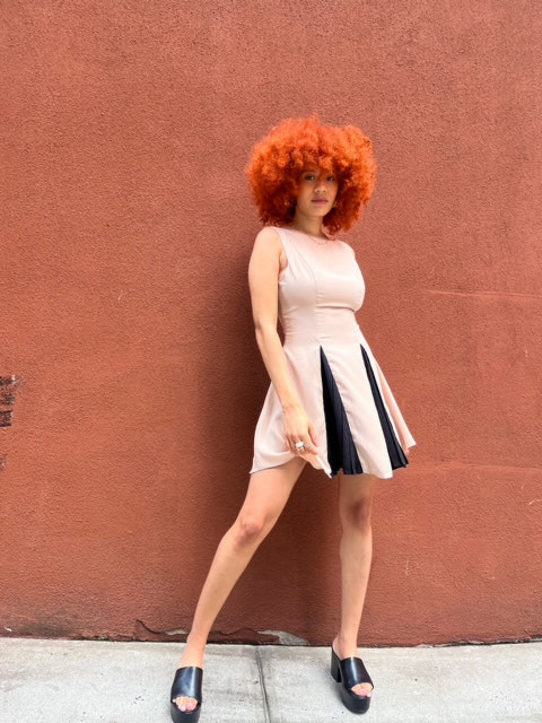 A sleeveless beige mini dress featuring a boat neckline and contrast black accents peeking through the pleats, creating a chic and versatile look suitable for any occasion. 