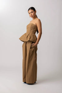Woman wearing a beige strapless peplum top and wide-leg pants on a white background