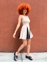 Load image into Gallery viewer, A sleeveless beige mini dress featuring a boat neckline and contrast black accents peeking through the pleats, creating a chic and versatile look suitable for any occasion. 
