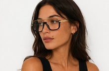 Load image into Gallery viewer, Black and gold oversized aviator-style optical frames with clear lenses, shown on a model and on a white background.
