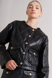 Person wearing a Glam Expressway black leather jacket with gold buttons on a plain background