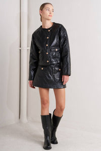Woman wearing a black leather jacket and skirt with black boots on a white background