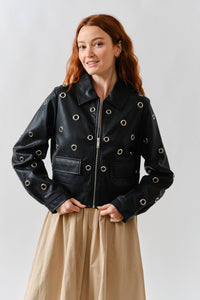Woman wearing a Glam Expressway black & silver leather jacket with grommets on a plain background