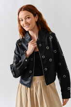 Load image into Gallery viewer, Woman wearing a Glam Expressway black leather jacket with grommets on a plain background
