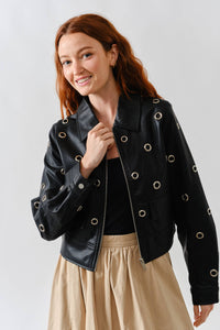 Woman wearing a Glam Expressway black leather jacket with grommets on a plain background