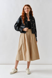 Woman wearing a Glam Expressway  black jacket, black top, beige skirt, and white sneakers on a white background