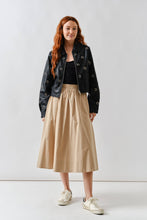 Load image into Gallery viewer, Woman wearing a Glam Expressway black jacket, black top, beige skirt, and white sneakers on a white background
