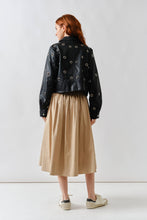 Load image into Gallery viewer, Person wearing a black jacket with circular patterns and a beige skirt on a white background
