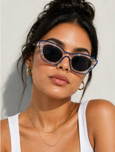 Load image into Gallery viewer, Woman wearing clear sunglasses with blue frames against a neutral background
