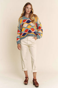 Woman wearing a colorful patterned sweater and white pants on a plain background