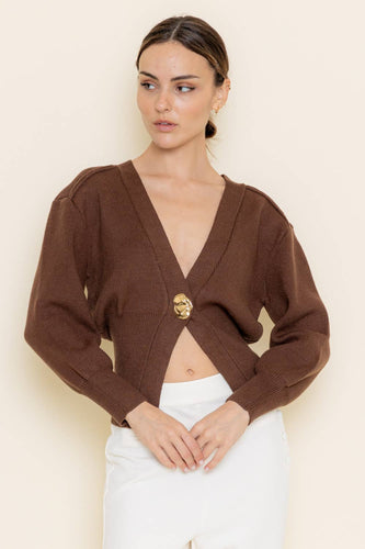 Woman wearing a brown cropped cardigan with a gold button on a beige background