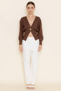 Woman wearing a brown cropped cardigan over a white top with a beige background