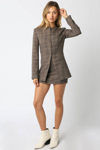 Woman wearing a plaid blazer and skirt set with white boots on a white background