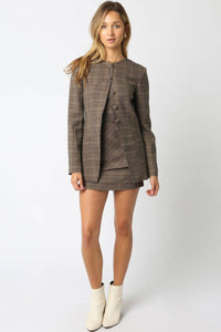 Woman wearing a plaid blazer and skirt set with white boots on a white background