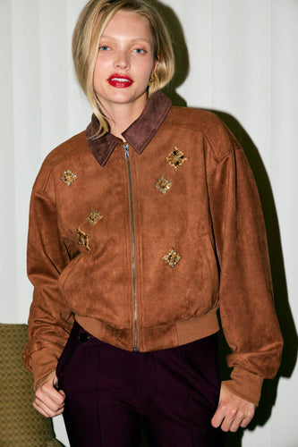 Woman wearing a brown suede jacket with decorative elements against a white background