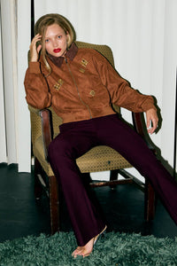 Woman sitting in a chair wearing a brown jacket with crystal embellised details and dark pants.