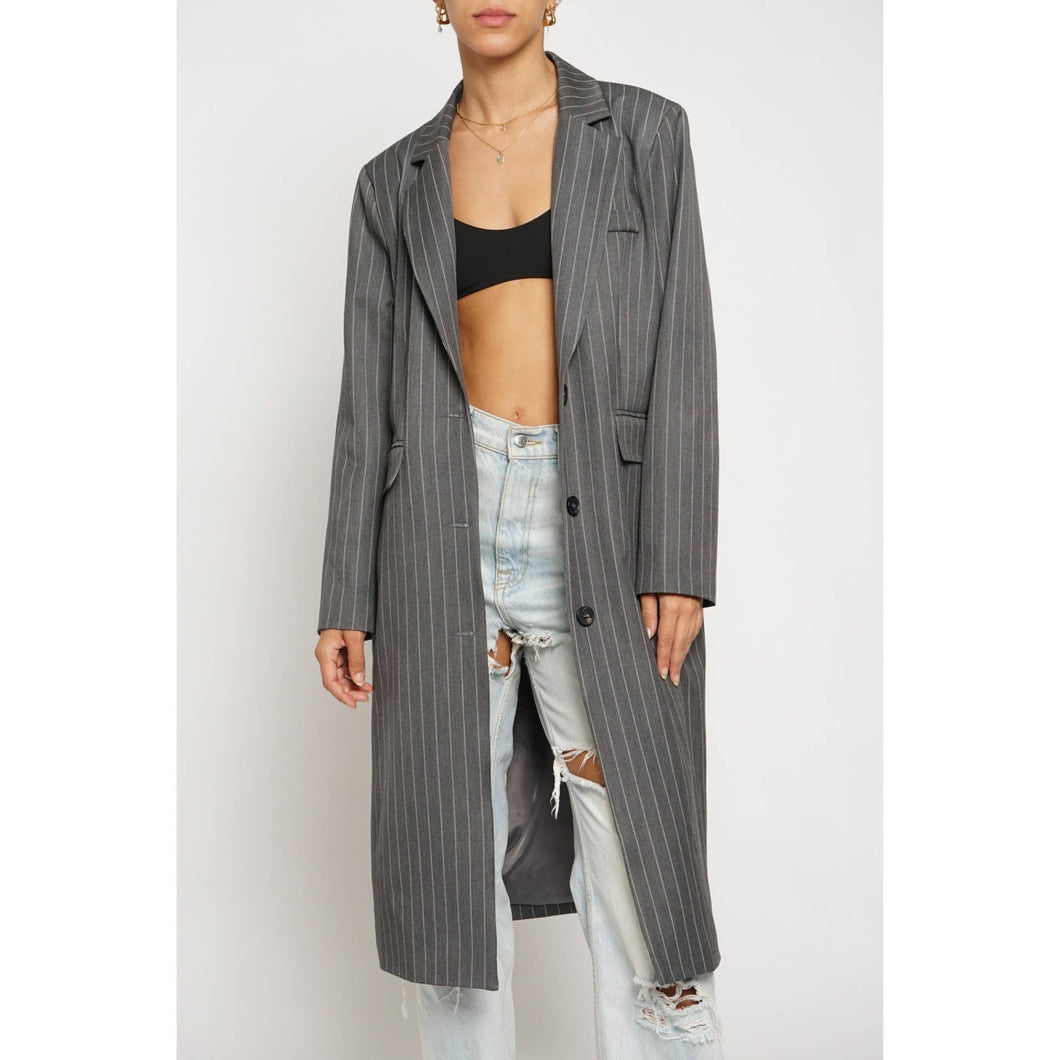 Person wearing a long gray pinstripe coat over a black crop top and light blue jeans on a white background
