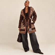 Load image into Gallery viewer, Model wearing a chocolate brown tapestry fringe cardigan with a self-tie waist belt and cream trousers.

