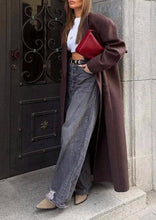 Load image into Gallery viewer, Person wearing a long brown coat, white shirt, and blue jeans, holding a red clutch.
