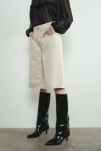 Load image into Gallery viewer, Person wearing beige denim long bermuda shorts and black knee-high boots against a white background
