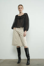 Load image into Gallery viewer, Woman wearing a black blouse, beige bermuda shorts, and black knee-high boots against a white background
