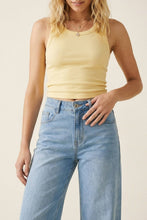 Load image into Gallery viewer, A woman wearing a pale yellow ribbed tank top and light blue high-waisted jeans, shown from the shoulders down against a plain beige studio background.

