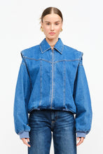 Load image into Gallery viewer, Model wearing an indigo denim bomber jacket with structured shoulders, zip-front closure, elastic hem, and gathered cuffs against a white background.
