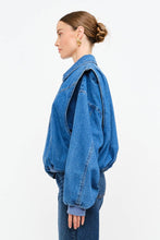 Load image into Gallery viewer, Model wearing an indigo denim bomber jacket with structured shoulders, zip-front closure, elastic hem, and gathered cuffs against a white background.

