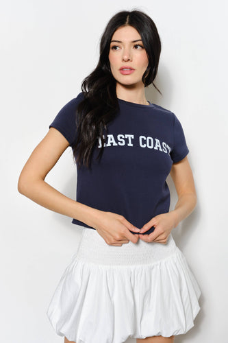 Woman wearing a navy blue t-shirt with 'East Coast' text and a white skirt on a light gray background