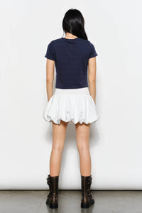 Person wearing a navy blue top and white skirt with black boots on a plain background