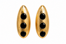 Load image into Gallery viewer, Gold-tone sculptural statement earrings with three glossy black circular accents displayed on a jewelry stand.
