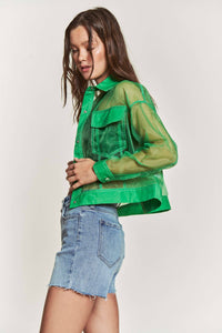 Woman wearing a green sheer jacket over a denim outfit on a white background