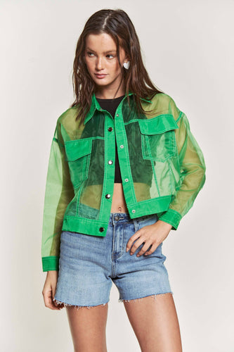 Woman wearing a green sheer jacket over a black top and denim shorts on a white background