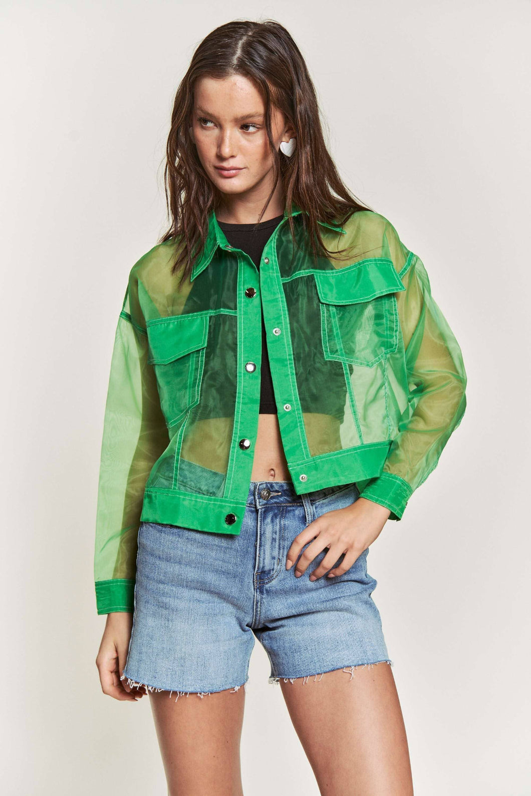 Woman wearing a green sheer jacket over a black top and denim shorts on a white background
