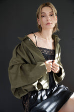 Load image into Gallery viewer, Person wearing a green jacket over a black dress against a dark background
