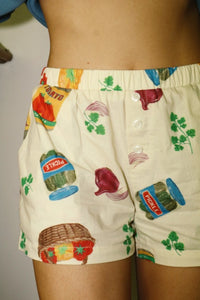 Cream high-waisted summer shorts with vibrant grocery and snack-themed print, lightweight woven fabric, and relaxed fit. A bold, playful statement piece for sunny days. Matching button-up shirt sold separately. Sold exclusively at Glam Expressway.