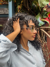 Load image into Gallery viewer, Model wearing oversized square green sunglasses with transparent frames and tinted lenses, posing in front of Glam Expressway Boutique in DUMBO, Brooklyn. Trendy summer eyewear offering UV protection and bold retro style.
