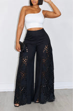 Load image into Gallery viewer, Black wide-leg pants with intricate cutout detailing along the sides, styled with a crop top on a model.
