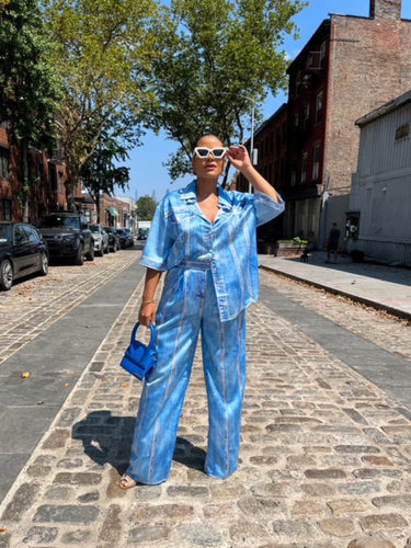 Boutique Owner wearing a blue satin denim printed outfit on a street with trees and buildings in the background in Dumbo Brooklyn