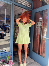 Load image into Gallery viewer, A model showcases a green checkered pleated mini dress with a box pleat design, exuding a blend of classic charm and contemporary style. The vibrant green check pattern adds a fresh pop of color, making it an ideal choice for spring and summer outings. The mini length and tailored fit highlight a playful yet sophisticated silhouette, perfect for casual gatherings, picnics, or brunches. 
